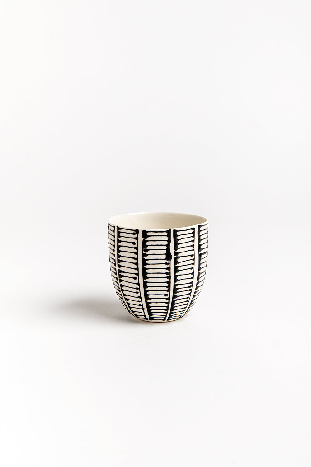 A white porcelain cup with black ladder stripes, hand-painted with geometric patterns.